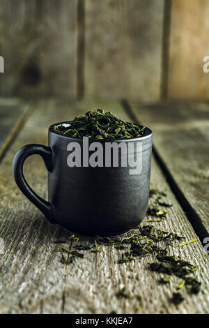 Dry organic green tea leafs in a black cup on a wooden background Stock Photo