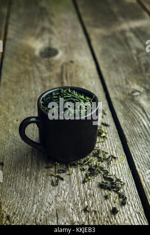Dry organic green tea leafs in a black cup on a wooden background Stock Photo