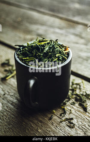 Dry organic green tea leafs in a black cup on a wooden background Stock Photo