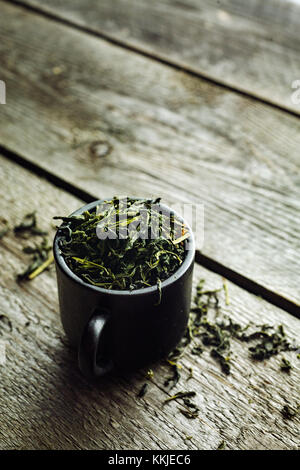 Dry organic green tea leafs in a black cup on a wooden background Stock Photo
