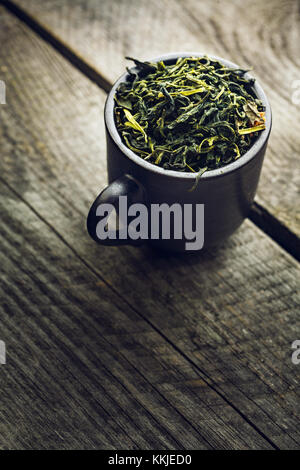 Dry organic green tea leafs in a black cup on a wooden background Stock Photo