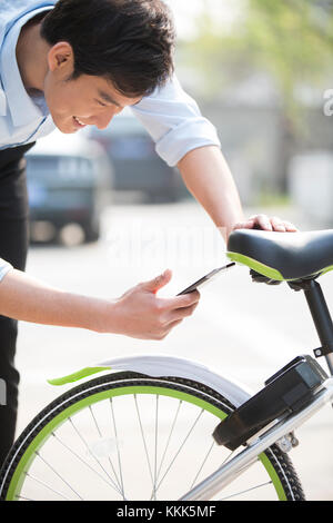Young Chinese man scanning a QR code to unlock a share bike Stock Photo