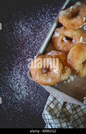 Homemade donuts with sugar and sugar powder in aluminum tray on checkered kitchen towel. Old metal background. Natural day light. Top view.  With copy Stock Photo