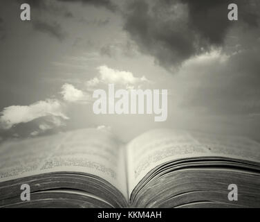 Detail of an old holy bible open with a beautiful and mystical sky in the background in black and white Stock Photo