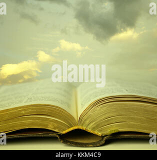 Detail of an old holy bible open with a beautiful and mystical sky in the background in a golden light Stock Photo