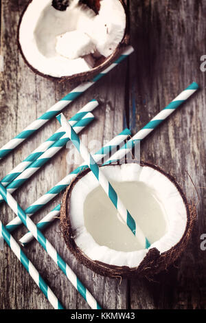 Broken coconut with coconut milk and vintage cocktail tubes on old wooden table in retro filter effect Stock Photo