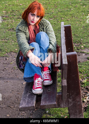 Redhead Girl on bench in park in autumn Stock Photo