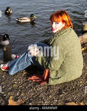 Beautiful girl in park feeding ducks in fall Stock Photo