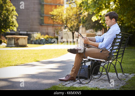 Businessman Outdoors Using Digital Tablet On Lunch Break In Park Stock Photo