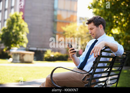Businessman Outdoors Using Mobile Phone On Lunch Break In Park Stock Photo