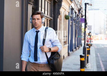 Businessman Wearing Wireless Headphones Walking To Work Stock Photo