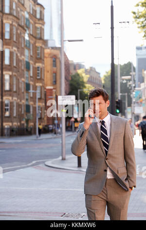 Businessman Talking On Mobile Phone Walking Along City Street Stock Photo