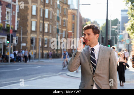 Businessman Talking On Mobile Phone Walking Along City Street Stock Photo