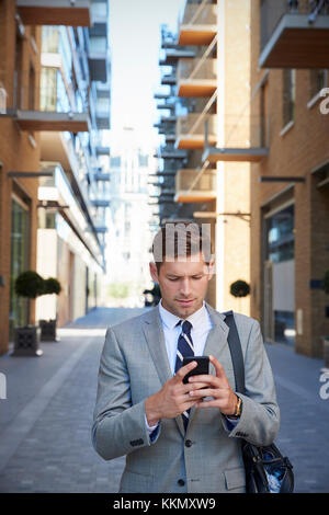Businessman Walking To Work In City Looking At Mobile Phone Stock Photo