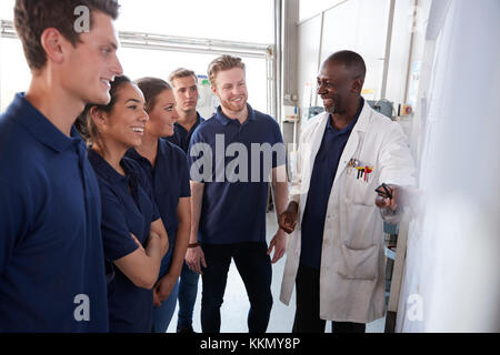 Smiling engineering apprentices gather round whiteboard at a training presentation, close up Stock Photo