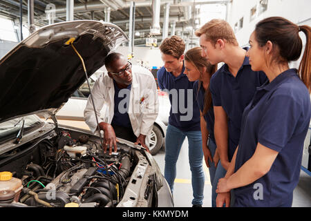 Mechanic instructing trainees around the engine of a car Stock Photo