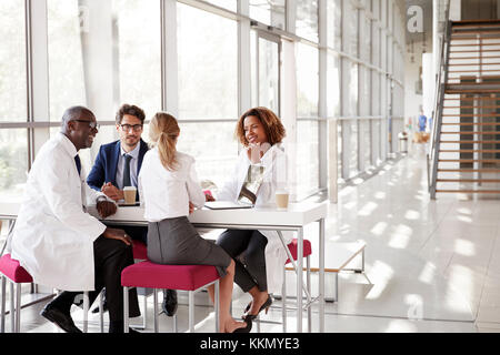 Four doctors talking at a table in a modern hospital lobby Stock Photo