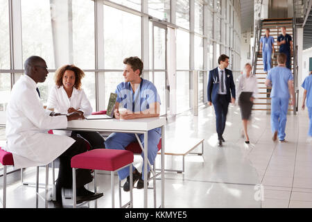 Three healthcare workers talking in a busy modern lobby Stock Photo