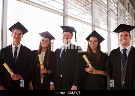 Five graduates in mortars and gowns holding certificates Stock Photo