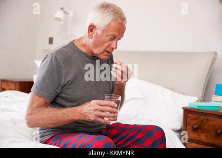 Senior Man Sitting On Bed At Home Taking Medication Stock Photo