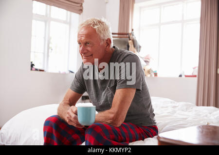 Senior Man Sitting On Side Of Bed With Hot Drink Stock Photo