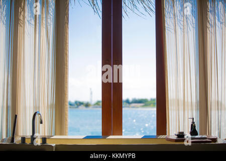 Inside an over water bungalow in a tropical island. The shot is from the inside and through the window there is the lagoon. There is a luxurious batht Stock Photo