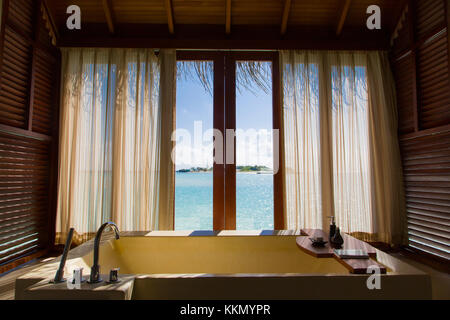 Inside the bathroom of an over water bungalow in a tropical island. The shot is from the inside and through the window there is the lagoon. There is a Stock Photo