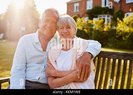 Senior Couple Sitting On Garden Bench In Evening Sunlight Stock Photo