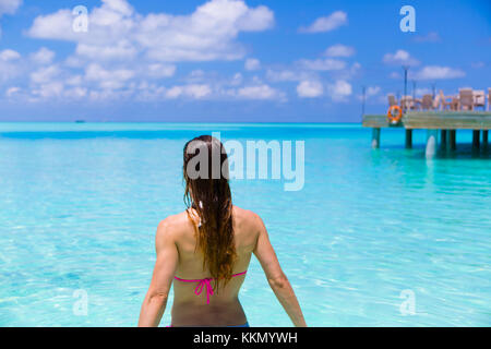 Rear view of a woman in the beach who is about to have a bath. Beautiful tones of blues and turquoises in the paradise. At background there is a jetty Stock Photo