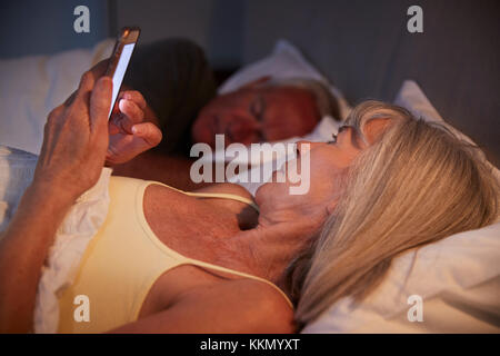 Sleepless Senior Woman In Bed At Night Using Mobile Phone Stock Photo