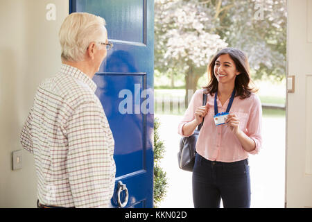 Senior man opens front door to young woman making home visit Stock Photo