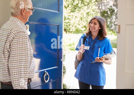 Female nurse showing ID to senior man at his front door Stock Photo