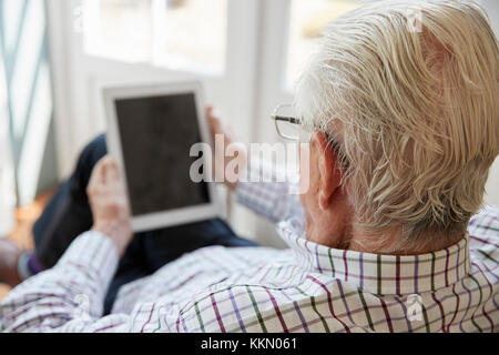 Senior man using tablet computer at home, over shoulder view Stock Photo