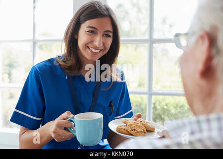 Nurse serves tea and biscuits to senior, over shoulder view Stock Photo