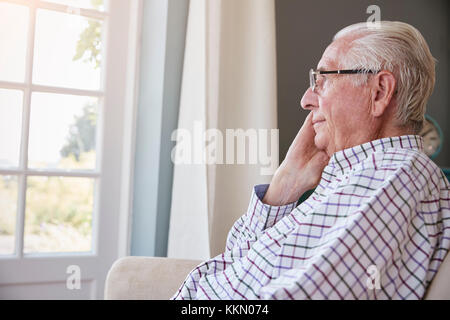 Senior man sits looking out of the window at home Stock Photo