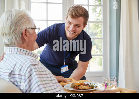 Male care worker serving dinner to a senior man at his home Stock Photo