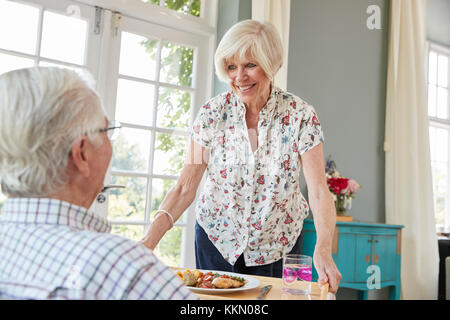 Senior woman serving dinner to senior man sitting at home Stock Photo