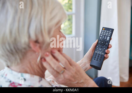 Senior woman using TV remote control, over shoulder view Stock Photo