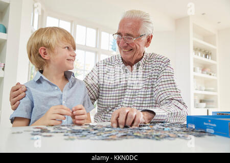 Senior man and grandson doing a jigsaw puzzle at home Stock Photo