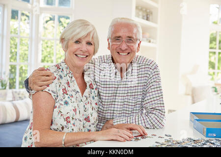 Senior couple doing a jigsaw puzzle at home, smiling to camera Stock Photo