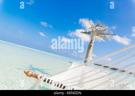 Hammock hold by a white tree in a shallow and clear sea on the lagoon in Maldives. Stock Photo