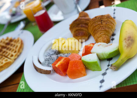 Delicious healthy breakfast outdoors in a wooden table with sea at background. The breakfast consists of fresh fruit and waffles with pancakes. Stock Photo