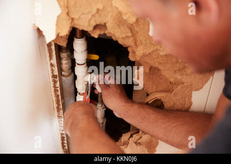 Over shoulder view of middle aged man repairing burst pipe Stock Photo