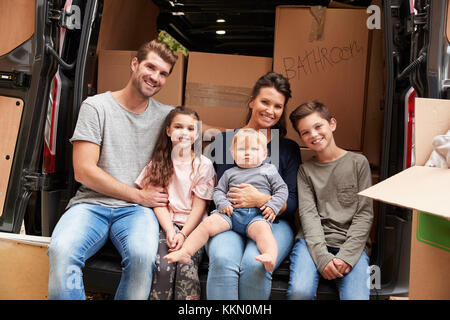 Family Sitting In Back Of Removal Truck On Moving Day Stock Photo