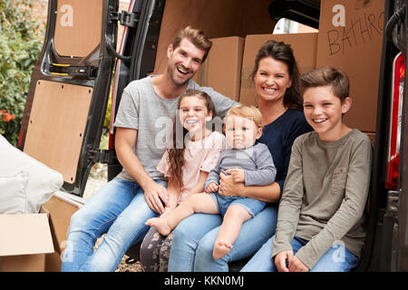 Family Sitting In Back Of Removal Truck On Moving Day Stock Photo