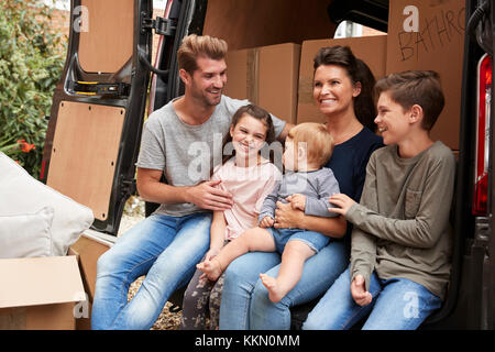 Family Sitting In Back Of Removal Truck On Moving Day Stock Photo