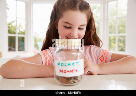 Girl Saving Pocket Money In Glass Jar At Home Stock Photo