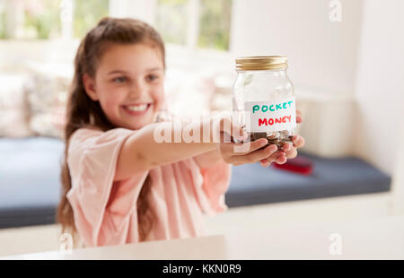 Girl Saving Pocket Money In Glass Jar At Home Stock Photo