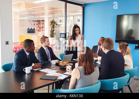 Female manager stands addressing colleagues in meeting room Stock Photo