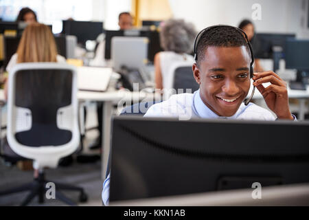 Young man working at computer with headset in busy office Stock Photo